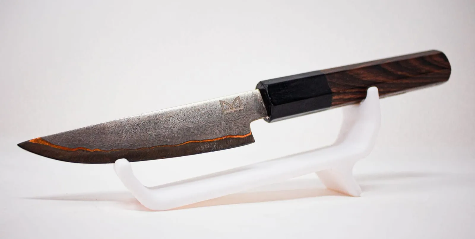 Cuchillo japonés de hoja damasco y mango octogonal de madera oscura sobre un soporte blanco