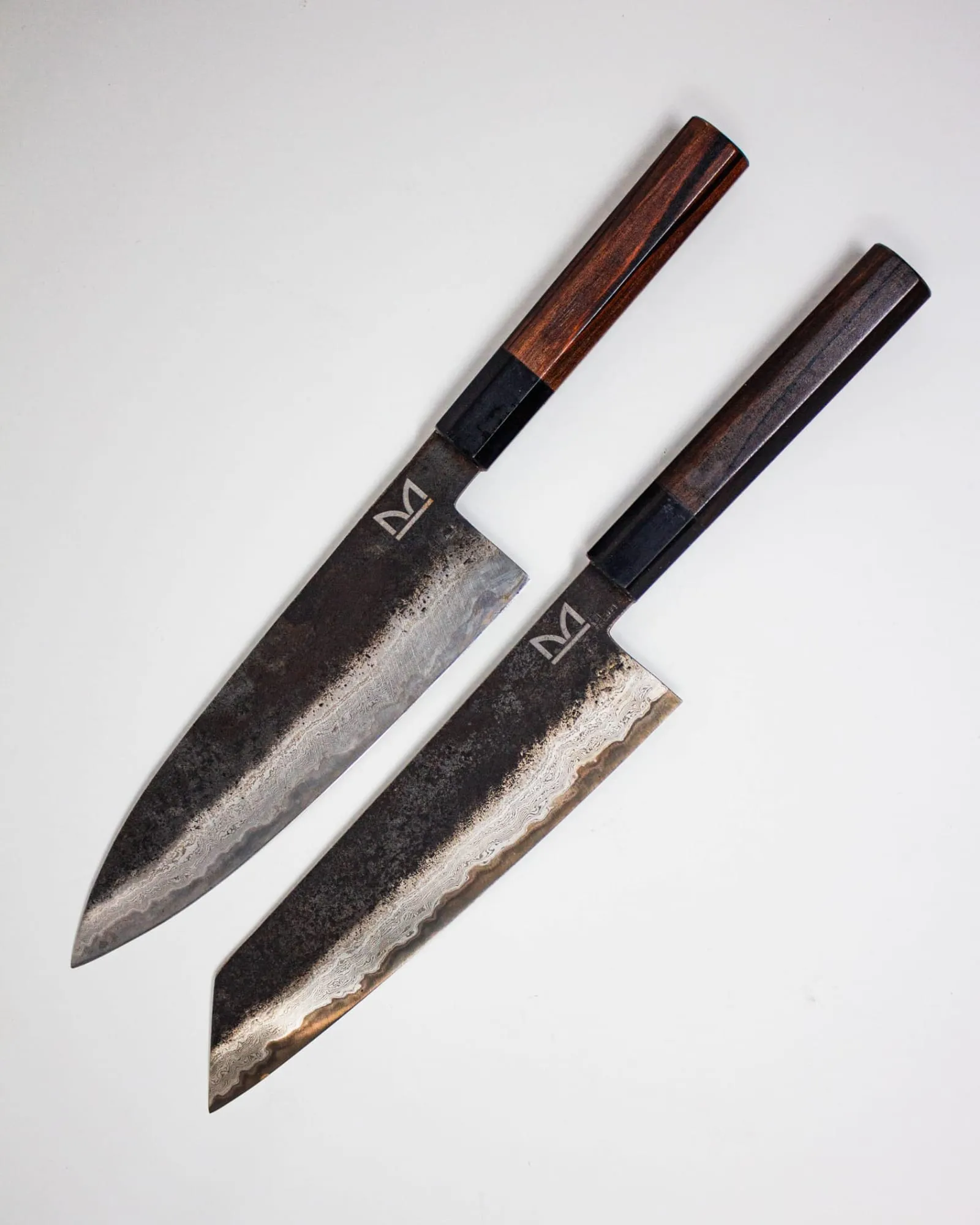 Dos cuchillos japoneses de hoja negra forjada y mango octogonal de madera, vistos desde arriba