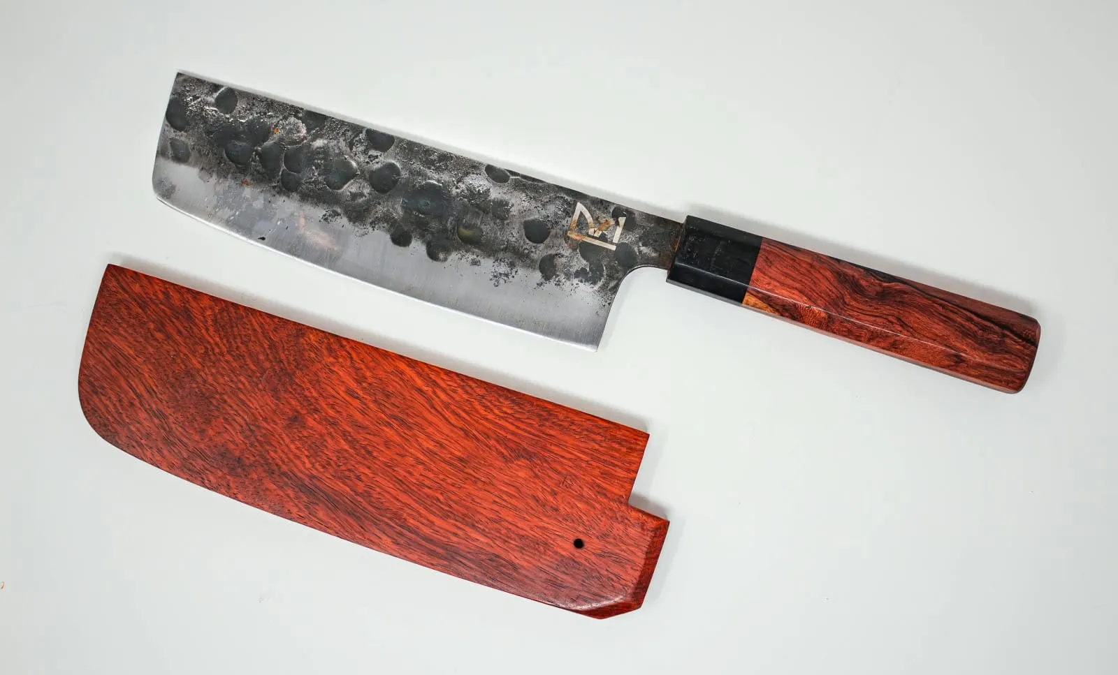 Cuchillo nakiri de hoja martilleada junto a su funda de madera rojiza