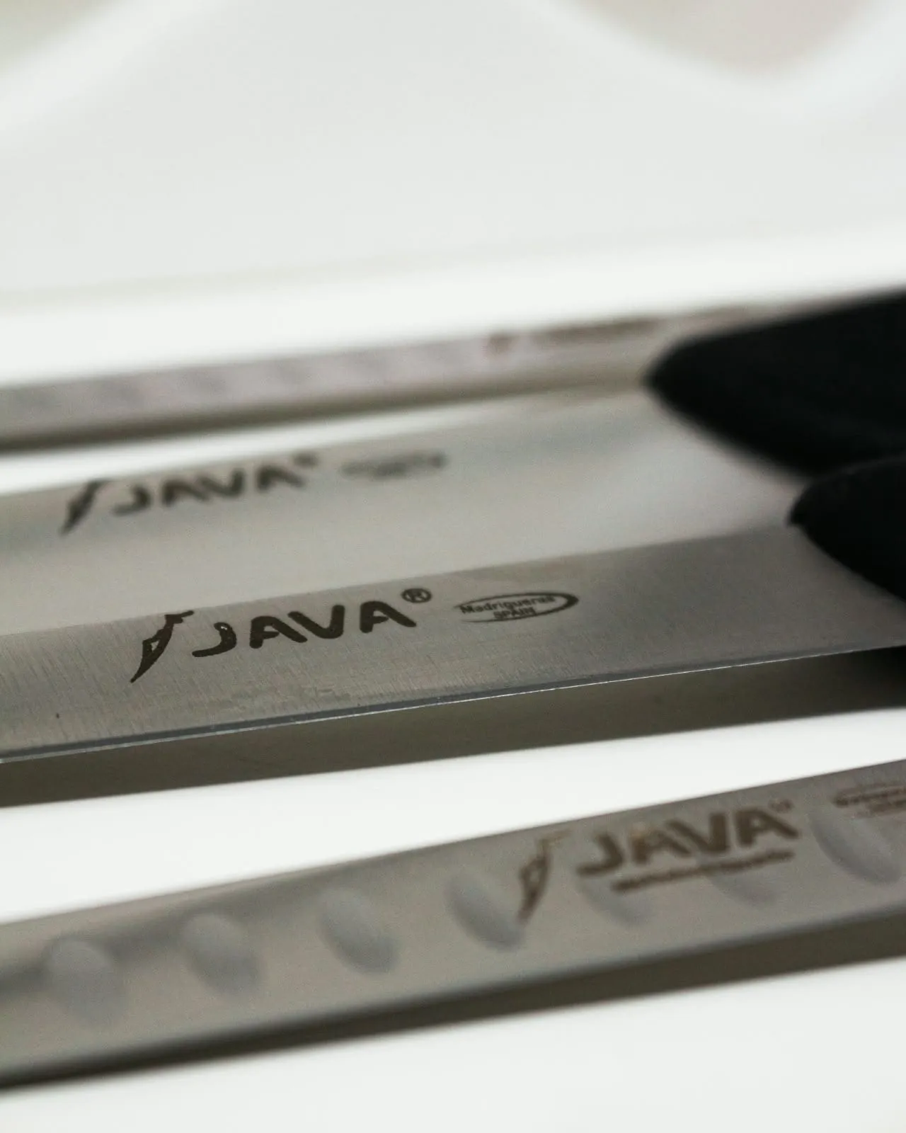 Detalle de tres hojas de cuchillo alineadas con la marca Java grabada en el acero