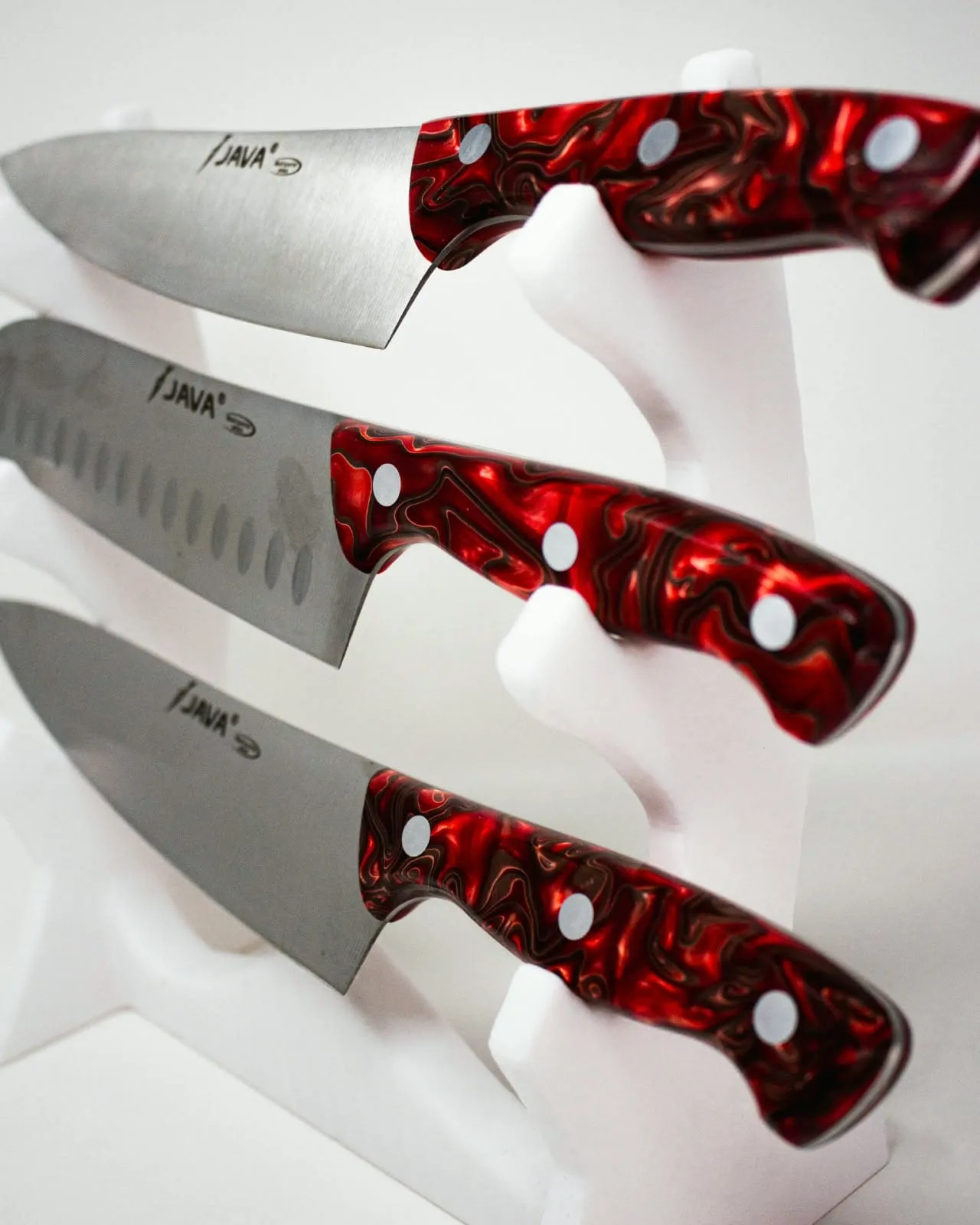 Detalle de las hojas de tres cuchillos con mango de resina roja, con la marca grabada junto al mango